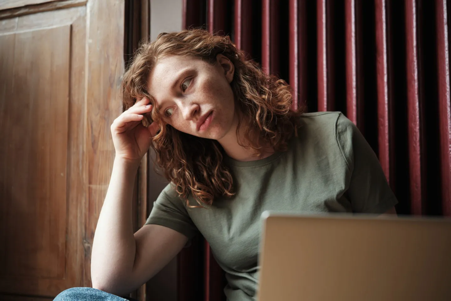 Young woman leans her head on her hand with a laptop in front of her