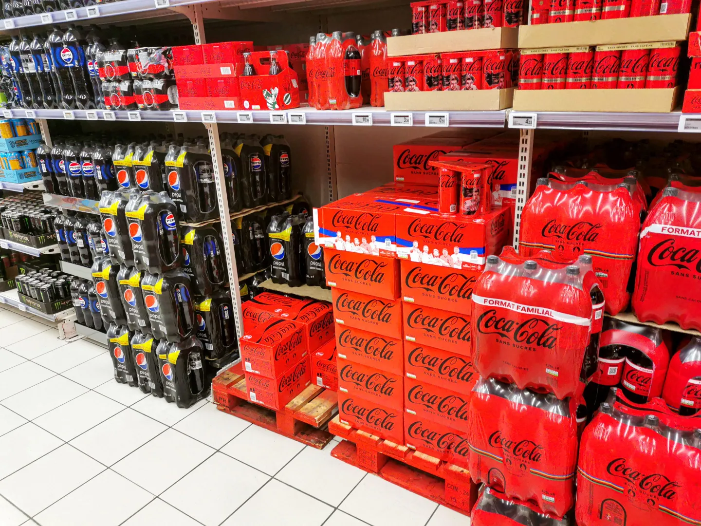 A display of plastic bottles and cans of various Coca Cola and Pepsi brand cola soft drinks