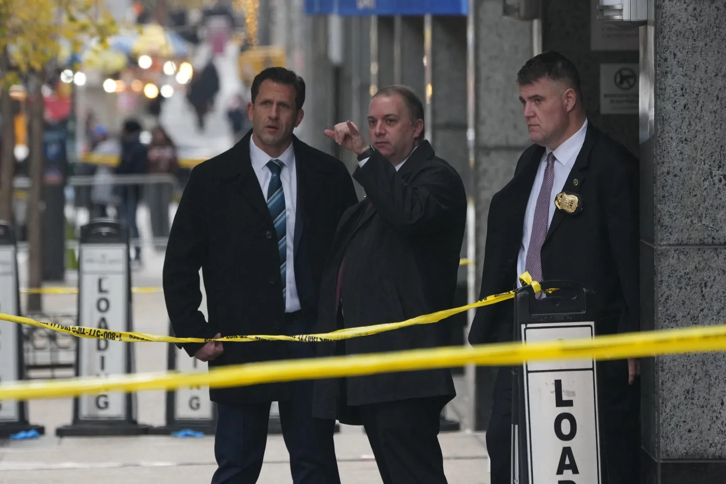 Men in suits stand behind yellow police tape outside a Manhattan hotel.