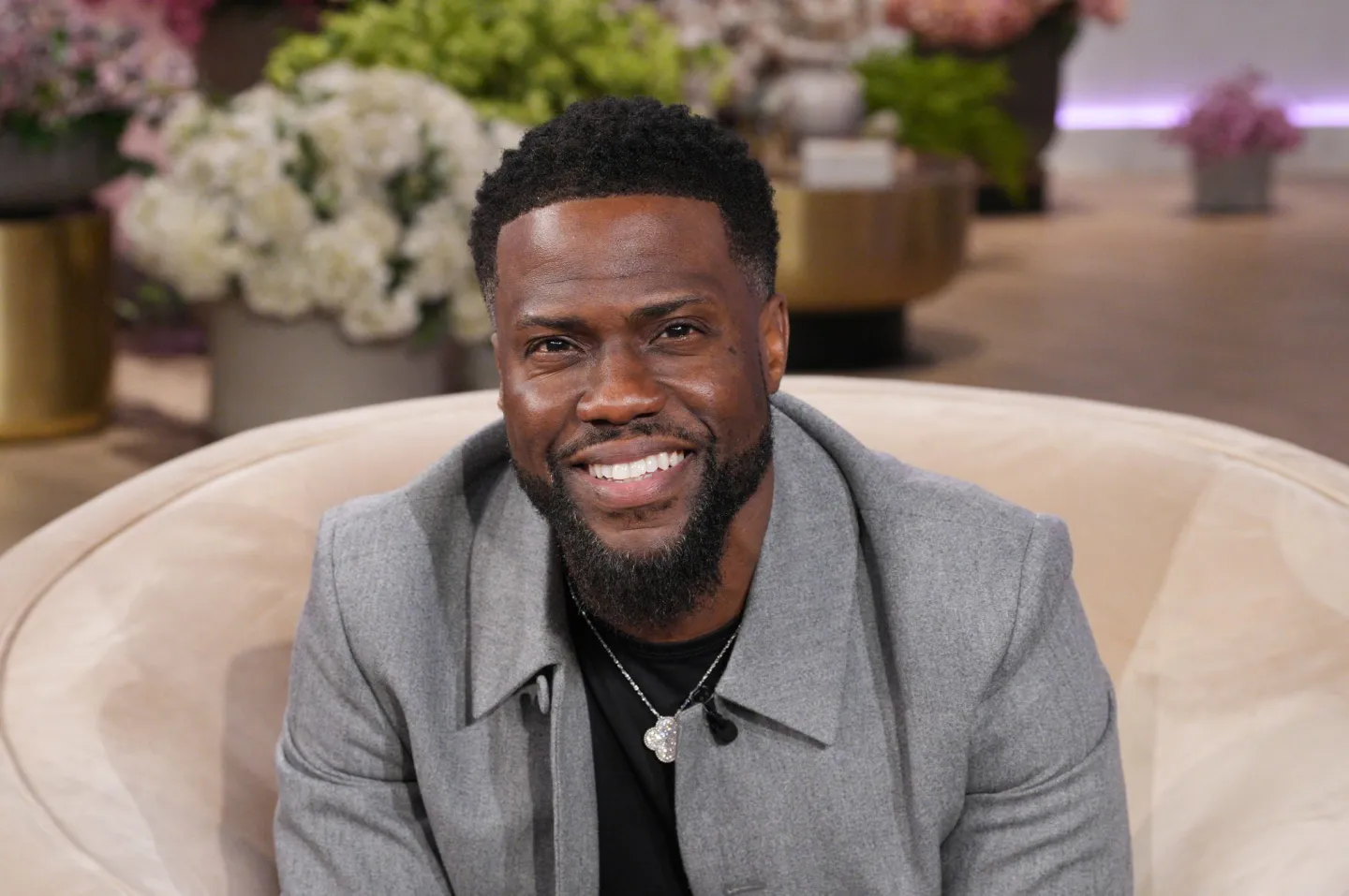 Kevin Hart sits in a chair and smiles for the camera