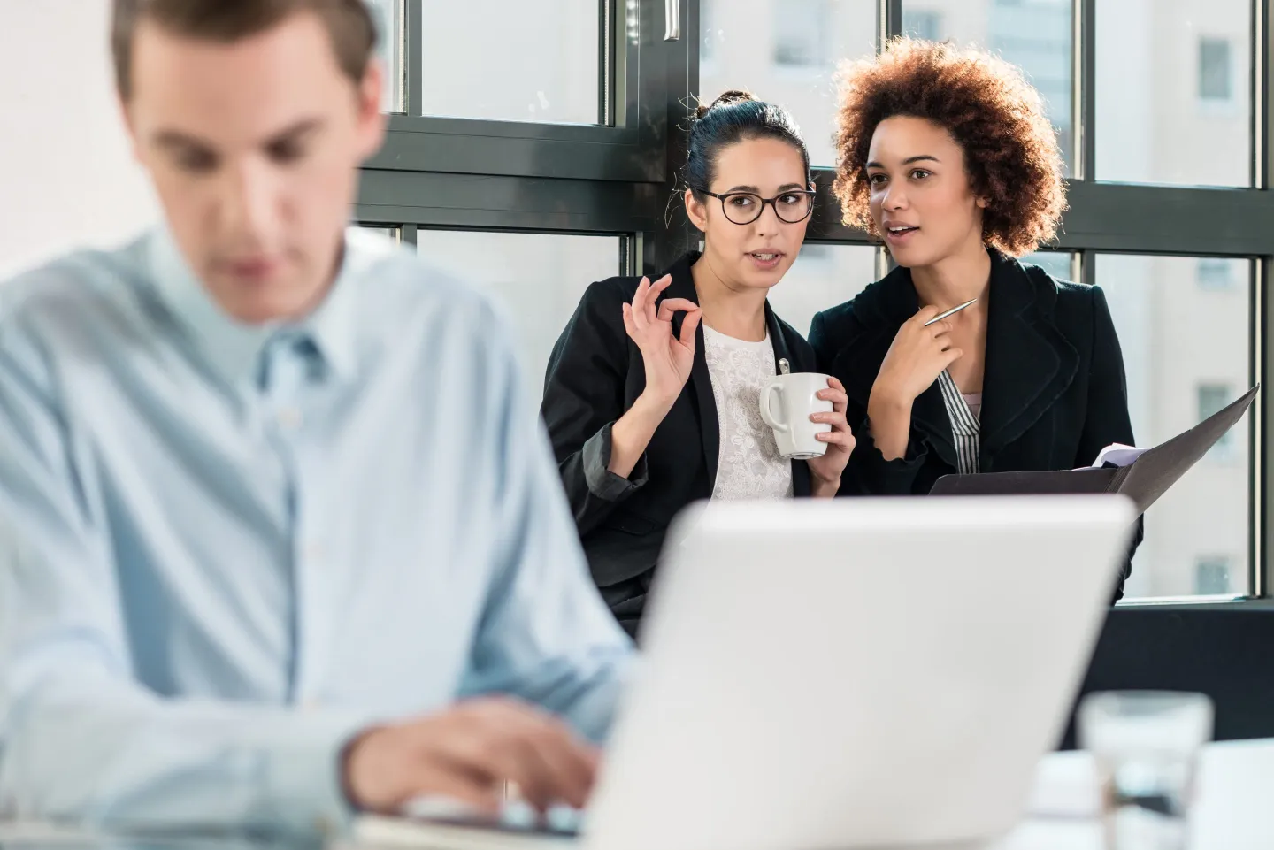 Two women whispering behind an office colleague's back