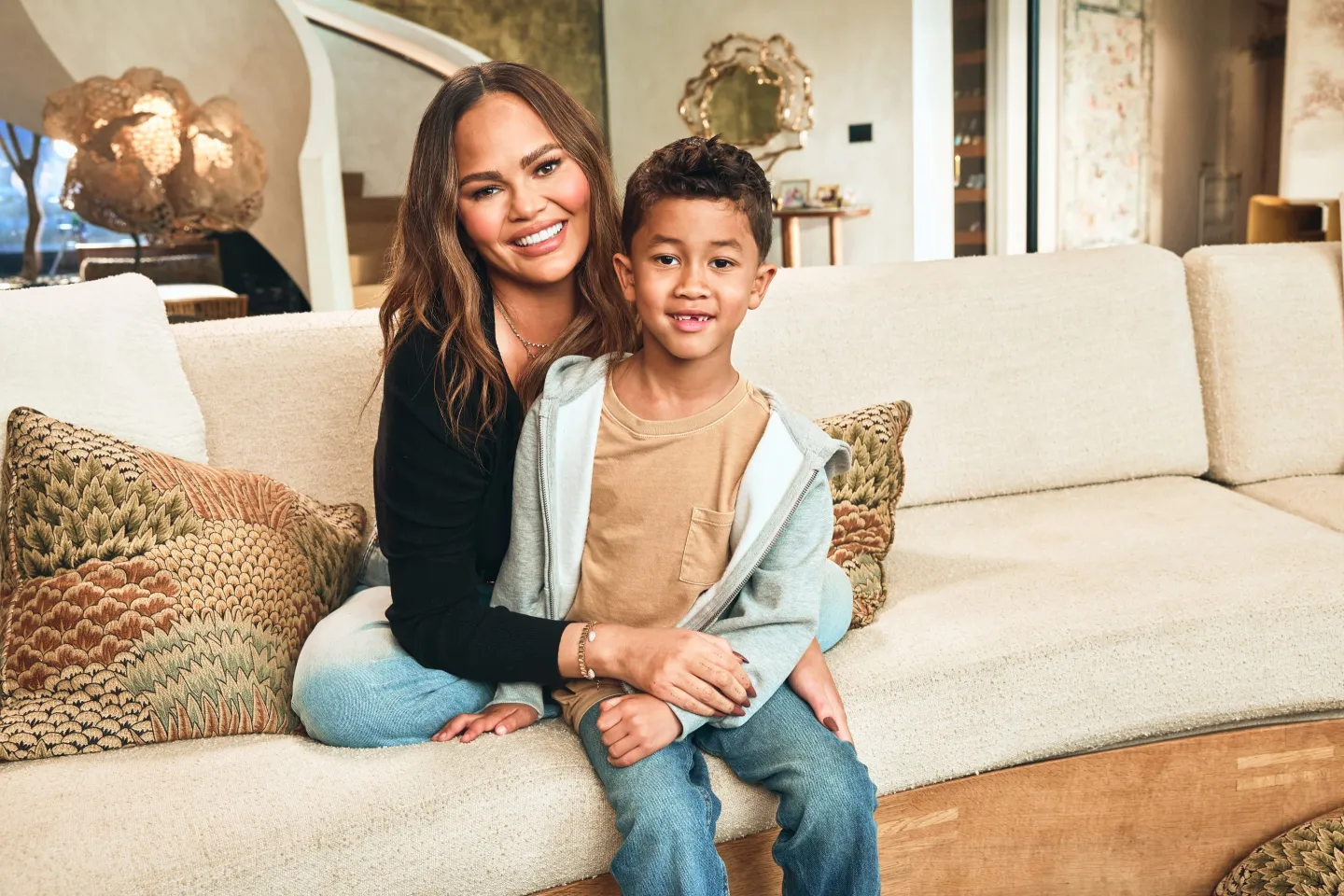 Chrissy Teigen sitting on a couch with her son Miles