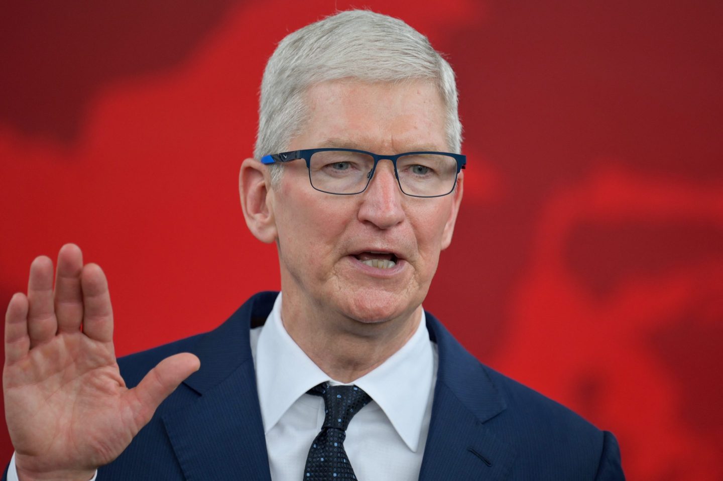 Tim Cook speaks, wearing a suit, against red background